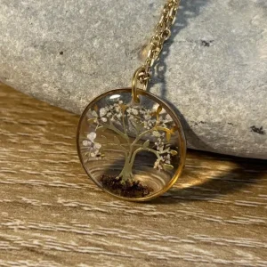 Collier artisanal arbre de vie avec inclusion de fleurs séchées et terre, pendentif rond présenté sur un galet